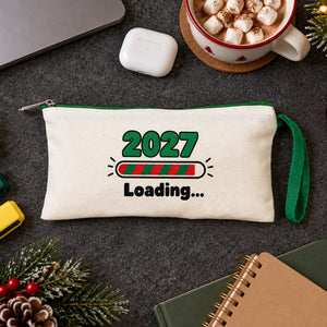 Cream pencil case with a green zipper and a 2027 Loading print on a study desk with highlighters, sticky notes and hot cocoa