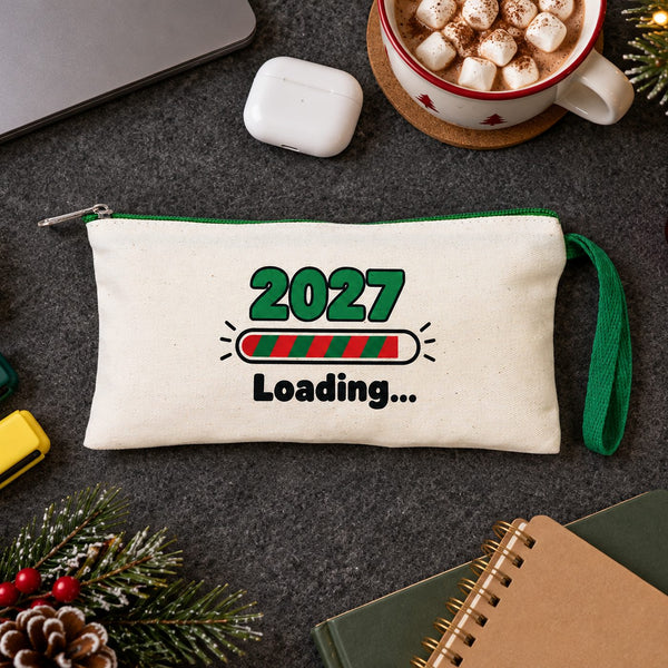 Cream pencil case with a green zipper and a 2027 Loading print on a study desk with highlighters, sticky notes and hot cocoa