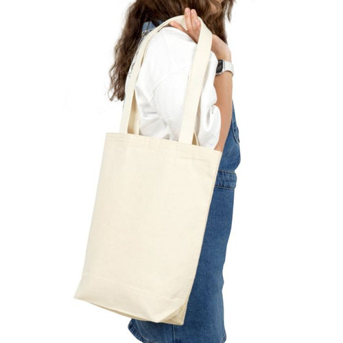 Person holding a beige tote bag on a white background