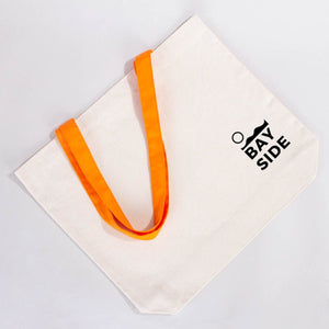 Beige tote bag with orange handles and 'Bay Side' text on a light gray background