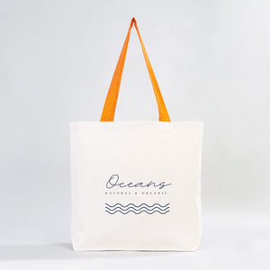 White tote bag with orange handles and 'Oceans' branding on a light gray background