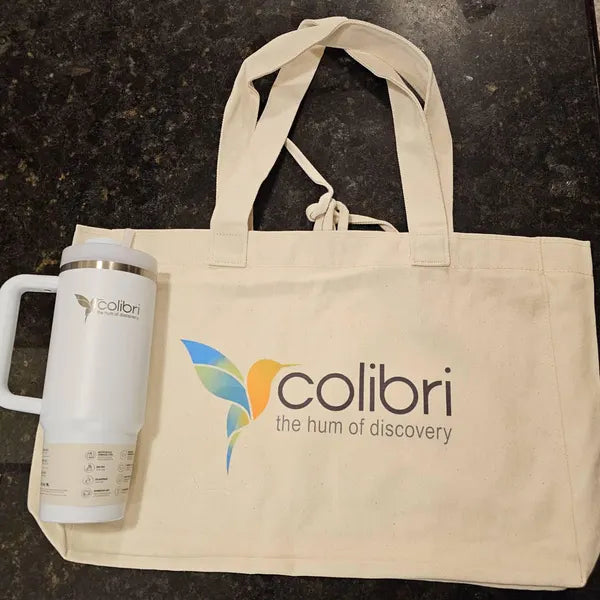Beige tote bag and white mug with Colibri logo on a dark surface