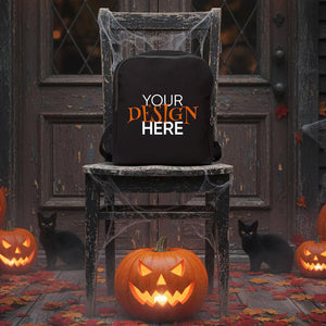 Black backpack with 'Your Design Here' text on a Halloween-themed background with pumpkins and cats.